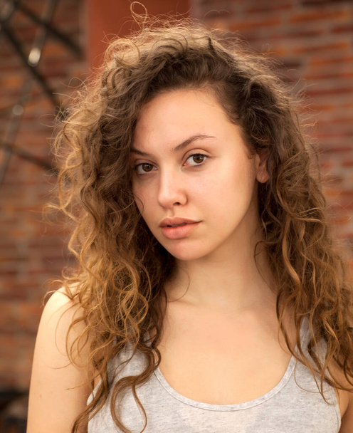 Mladá dívka s kudrnatými vlasy bez make-upu póza uvnitř - Fotografie, Obrázek