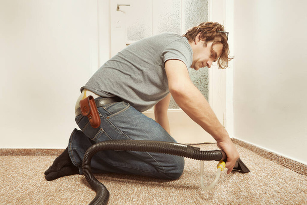 Caucasian man cleaning deeply carpet with wet and dry vacuum hand adapter  - 写真・画像