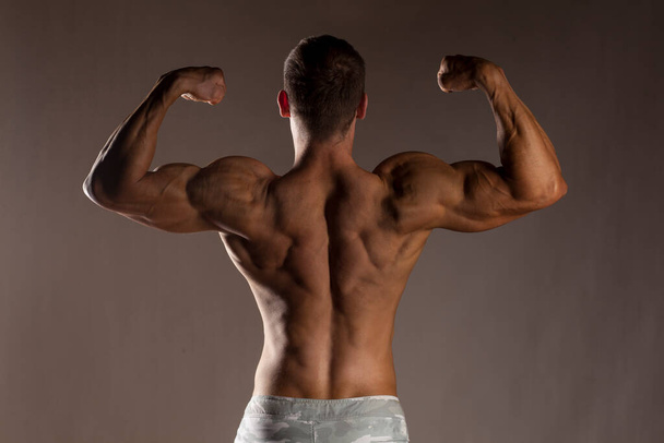rear view of the half-naked handsome and muscular young man posing on a gray background - Photo, Image