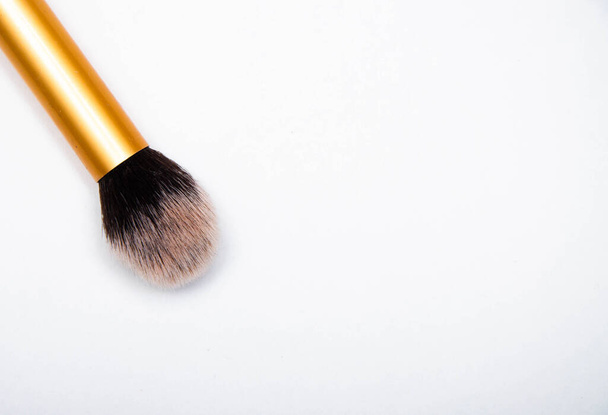 Большая пушистая кисть для макияжа с золотой ручкой и черным краем. Кисть лежит на белом фоне в макросах
 - Фото, изображение