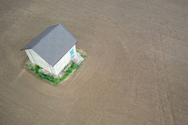 Μια αγροικία, μια αποθήκη ή ένας αχυρώνας, ανάμεσα σε ένα άδειο χωράφι. Θέα από το drone. - Φωτογραφία, εικόνα