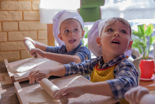 Close up portrait of two little boys in cook hats rolling pizza dough - Fotoğraf, Görsel