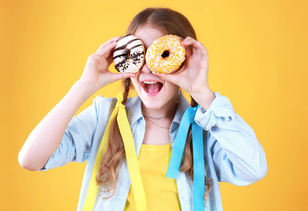 Child with donuts eyes on yellow background,kid and doughnuts have a fun.Girl positive emotions portrait.Happy childhood. - Foto, imagen