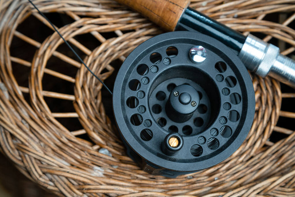 Close up of fly fishing rod with reel next to braided basket. Fly fishing equipment still life. Nobody - Fotoğraf, Görsel