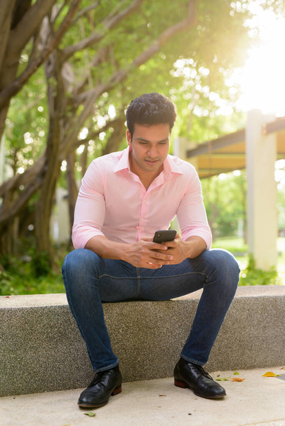 Portrait of young handsome Indian businessman relaxing at the park outdoors - Photo, Image