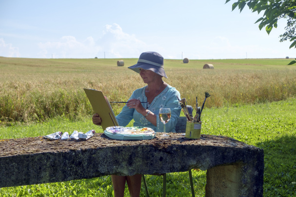 Umělkyně sedí v pozdním odpoledním stínu s venkovským výhledem na krajinu a pracuje na malbě, kterou začala dříve během dne. - Fotografie, Obrázek