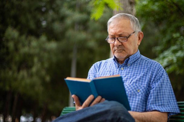 Um homem idoso está sentado no banco e lendo um livro
 - Foto, Imagem