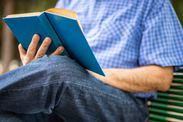 Yaşlı bir adam bankta oturuyor ve kitap okuyor. - Fotoğraf, Görsel