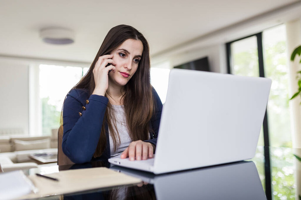 Young woman working from home, using mobile phone and laptop at the desk. Online meeting concept. - Foto, imagen