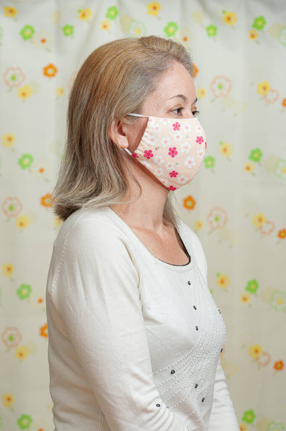 Портрет жінки середнього віку, одягненої в маску тканини DIY для захисту від коронавірусу (COVID-19) та інших інфекційних захворювань. Квіткова завіса. Дивлячись збоку. - Фото, зображення