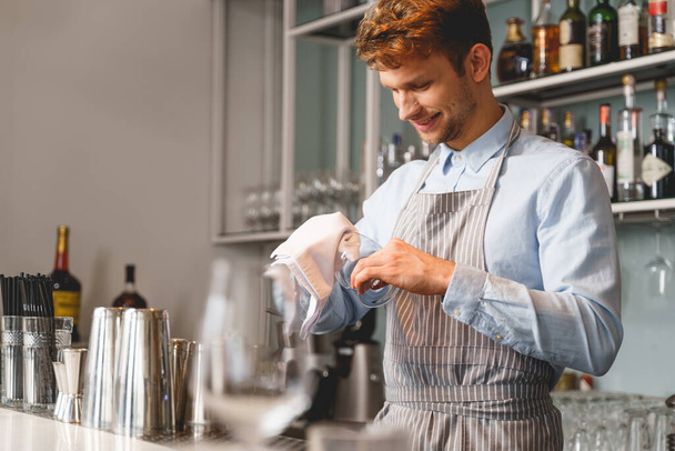 Cheerful bartender wiping glass with special rag - Foto, Imagem
