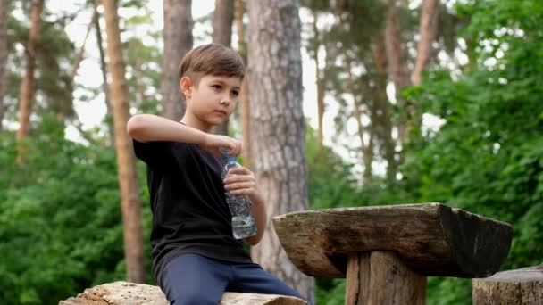Malý chlapec pije vodu z láhve po sportu. Odpočinek dítěte po spuštění. - Záběry, video