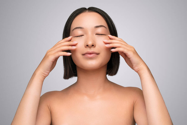 Asian woman touching cheeks under closed eyes - Foto, Imagem