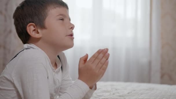 vertrouwen in God, gebed mannelijk kind met hoop in zijn hart en met gevouwen armen, bidt tot God op wielen in de buurt van bedstede - Video