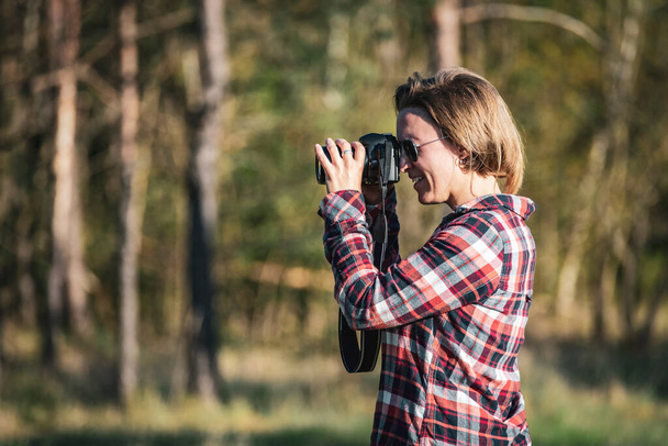 Young female photographer taking a photo outdoors in the woods in warm eventing light - Foto, imagen