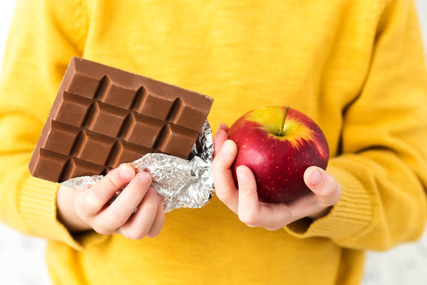 woman holding chocolate bar with a red apple - Фото, изображение