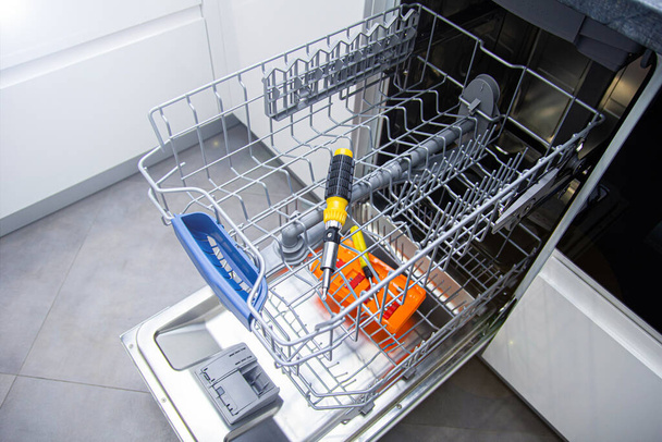 repair of a modern dishwasher with screwdrivers in the kitchen - Foto, Bild