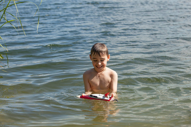 Kleiner Junge spielt mit einem Boot im See - Foto, Bild