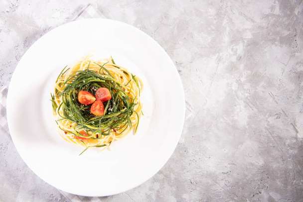 Spaghetti with agretti, a spring vegetable from Italy, on a white plate on a gray background, above - Zdjęcie, obraz