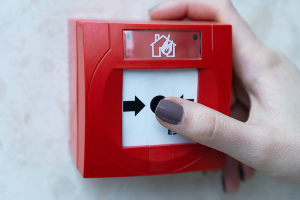 Human hands are pulling red fire alarms on the white walls along the mall corridor.The concept of a picture about fire alarms in buildings. Fire extinguish equipment. Pressing the fire alarm system. - Photo, Image