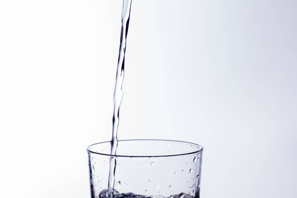 Čirá pitná voda padá do čiré sklenice, zdravé, zdravé, sladké vody bez zápachu nebo chuti. Po hladině stékaly kapky vody. Proud vody vstupující do skla - Fotografie, Obrázek