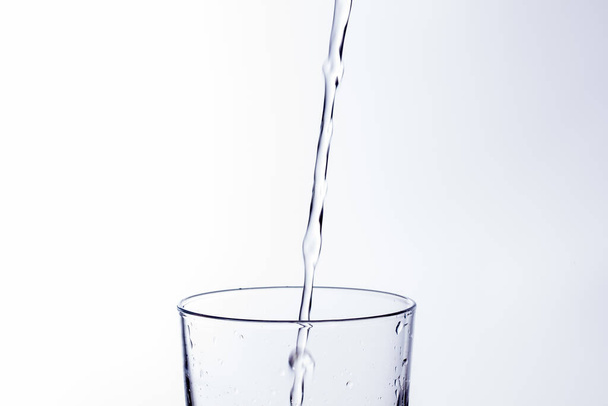 Tiszta, ivóvíz esik egy tiszta pohár, egészséges, egészséges, friss víz szaga és íze nélkül. Vízcseppek fröccsennek a felszínre. Az üvegbe belépő víz sugara - Fotó, kép