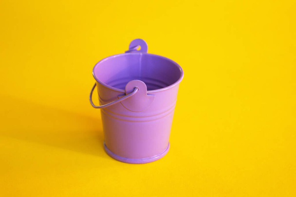 Miniature empty lilac bucket lies on a bright yellow background. - 写真・画像