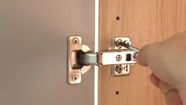 Close up male hand untightens screw with screwdriver on a polished stainless door hinge on a cabinet door. Craftsman repairing home furniture. - Footage, Video