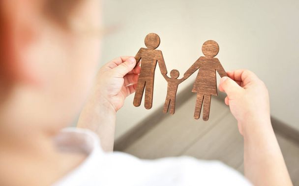 The little child looking on the wooden figures of mom, dad and child in his hands. Concept of the child dreaming about family - Fotoğraf, Görsel
