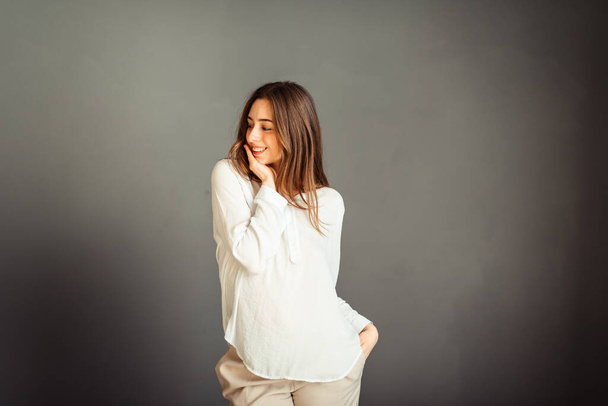 Молодая девушка в белой рубашке на сером фоне. Французская женщина в белой блузке на фоне серых стен. Без ретуши и грима
. - Фото, изображение