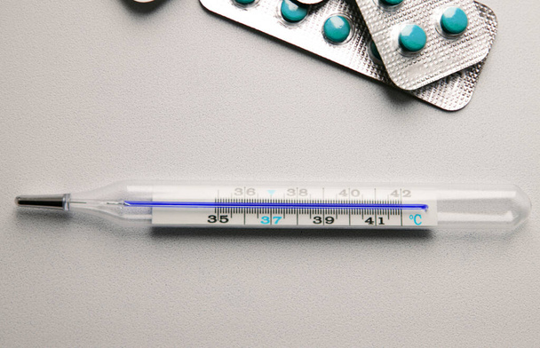 barevné pilulky a lékařské teploměr na bílém pozadí zblízka - Fotografie, Obrázek