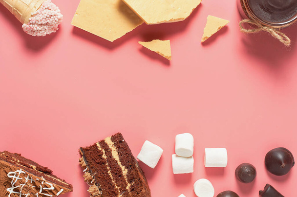 Stücke Schokoladenkuchen neben verschiedenen Süßigkeiten liegen auf einem rosafarbenen Tisch. Kopierraum. Ansicht von oben - Foto, Bild