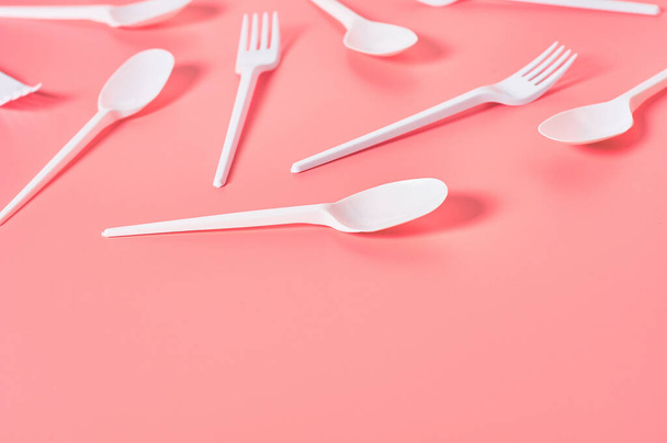 White disposable spoons and forks scattered on pink background. Concept of save environment, ecology, recreation on picnic, party and other events. Copy space - Photo, Image