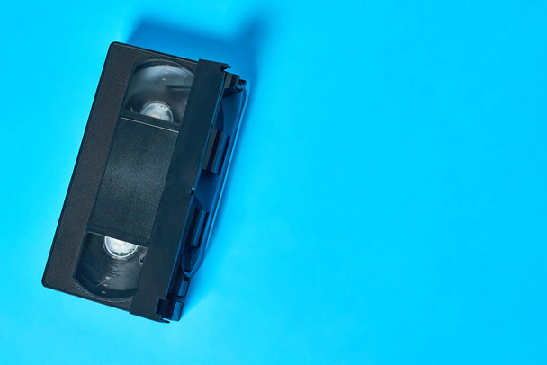 Single black old plastic vhs video cassette lies on blue desk. Concept of 90s. Copy space. Top view - Foto, Imagem