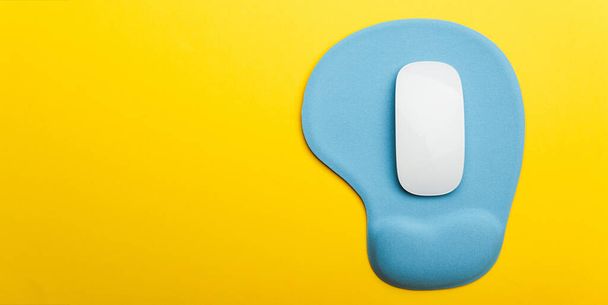 Top view flat lay of blue pad or mousepad with wireless white computer mouse modern design isolated on a yellow background and copy space - 写真・画像