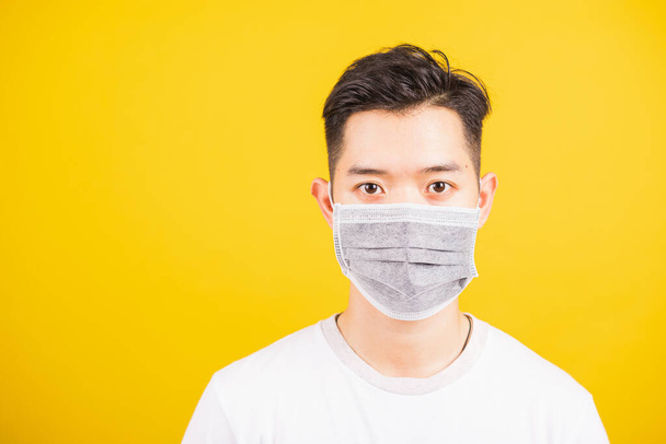 閉鎖アジアの若い男は顔マスク保護生殖ウイルスや空気のほこりを身に着けています,スタジオは黄色の背景とコピースペースに隔離されたショット,医学発生コロナウイルスCOVID-19の概念 - 写真・画像