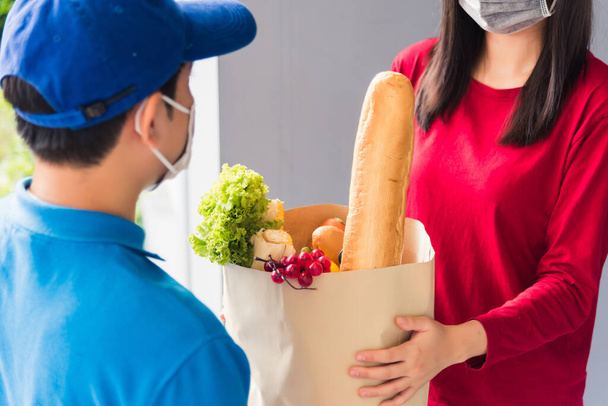 Asian young delivery man in uniform wear protective face mask he making grocery service giving fresh food to woman customer receiving front house under pandemic coronavirus, Back to new normal concept - Fotoğraf, Görsel