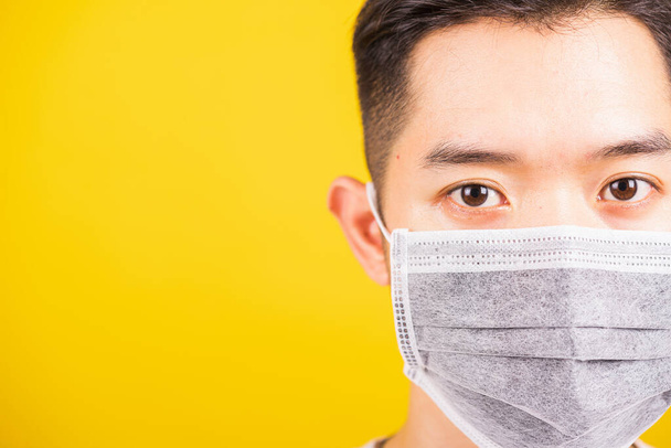 Closeup Asian young man wearing face mask protective germ virus or air dust, studio shot isolated on yellow background and copy space, medical outbreak coronavirus COVID-19 concept - 写真・画像
