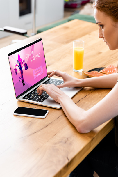 Nainen käyttää kannettavaa tietokonetta verkkokaupoissa verkkosivuilla lähellä älypuhelin ja aamiainen pöydällä  - Valokuva, kuva