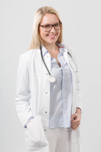 young smiling female doctor in doctor's overall with stethoscope in front of neutral background - 写真・画像