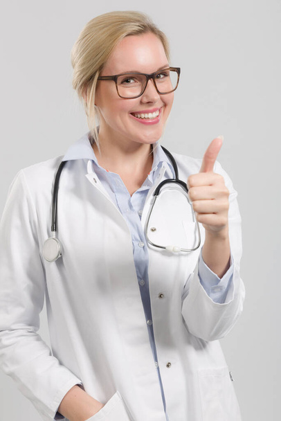 jonge vriendelijke vrouwelijke arts in het algemeen arts met stethoscoop toont duimen omhoog - Foto, afbeelding