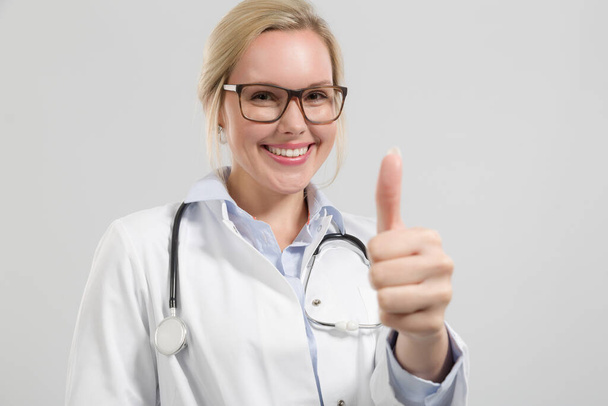 young friendly female doctor in doctor's overall with stethoscope shows thumbs up - Foto, immagini