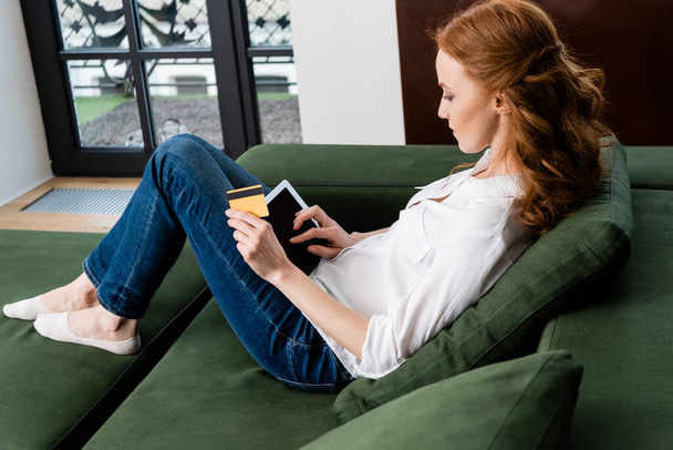 Side view of woman using digital tablet and credit card on couch  - Foto, Imagen