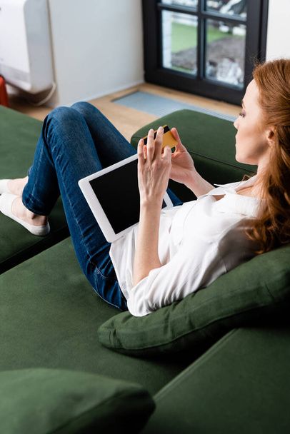 Enfoque selectivo de la mujer que sostiene cad de crédito y tableta digital en el sofá en casa
  - Foto, imagen