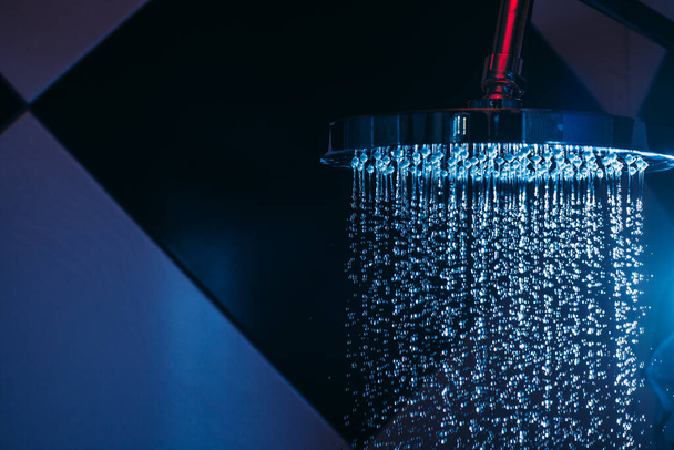 Gotas de agua caen de una regadera en la ducha con luz azul. Gotas de agua en primer plano. Flujo de agua. Gran regadera redonda
. - Foto, imagen