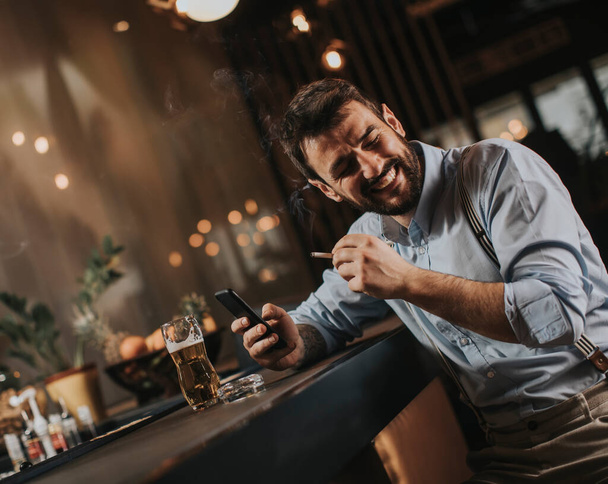 Mladý muž pije pivo a kouří cigarety v hospodě - Fotografie, Obrázek