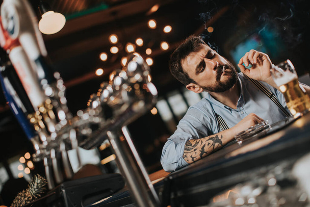 Junger Mann trinkt Bier und raucht Zigarette in Kneipe im Nachtclub - Foto, Bild