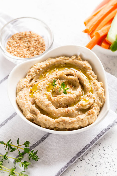 hummus sauce in a bowl, sesame seeds, olive oil, cucumber and carrots on a light background - Photo, Image