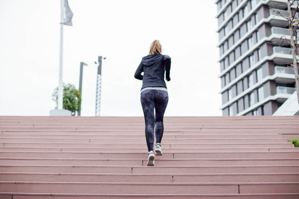 Genç bir kadın şehir merdivenlerinde koşuyor ve müzik dinliyor. - Fotoğraf, Görsel