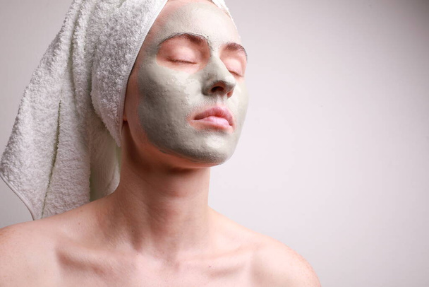 Beautiful young woman with facial mask on her face. Skin care and treatment, natural beauty and cosmetology concept. - Foto, imagen